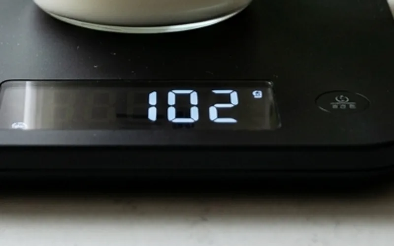 Digital kitchen scale displaying 102g for 100 mL milk